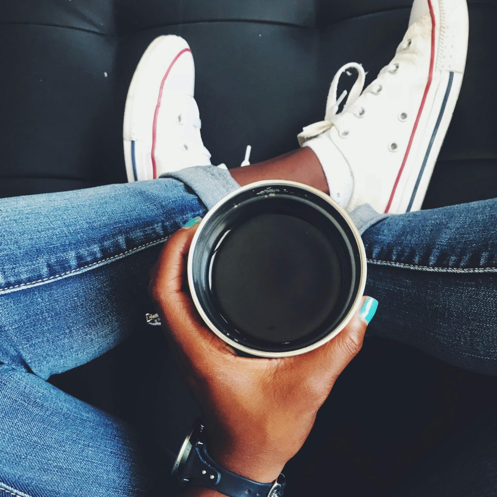 Top view of a person holding coffee while wearing jeans and white sneakers.